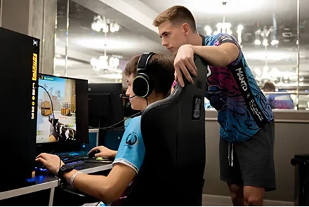 Egy edző figyeli és segíti a számítógépen játszó e-sport játékost edzés közben.